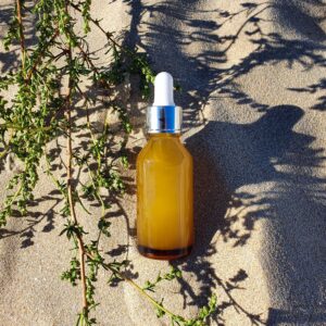 Glass cosmetic bottle with dropper pipette and herbs shadow on the sand texture background. Beauty product for facial skin care, bottle for branding of medicine or cosmetics. Natural organic cosmetics